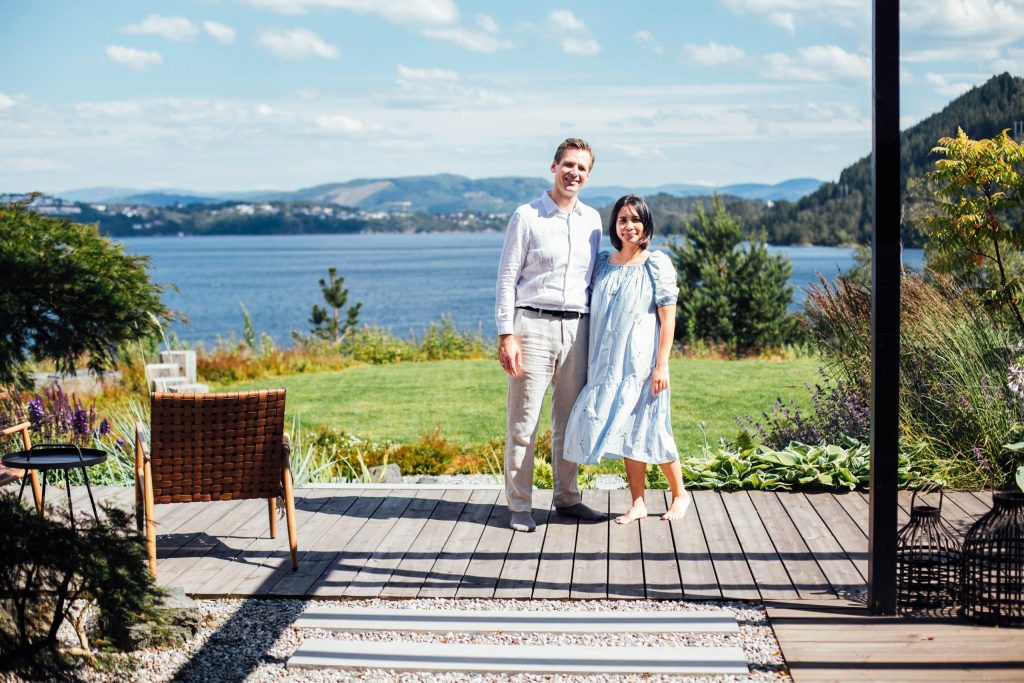 En mann og en kvinne som går mot kamera med sjøen i bakgrunnen. Begge går kledd i lyse farger.